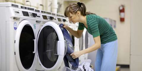 Woman in laundromat loading clothes into washing machine
