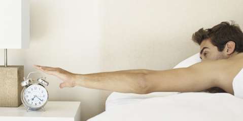 Young guy in bed putting off the alarm clock