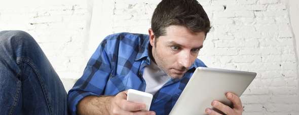 young man at home couch working with mobile phone and digital tablet