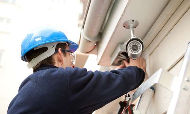 A man carefully placing surveillance cameras outside a building.